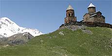 Klosterkirche mit Schutzwall in einer Berglandschaft, grüne Wiesen und im Hintergrund schneebedeckte Berge